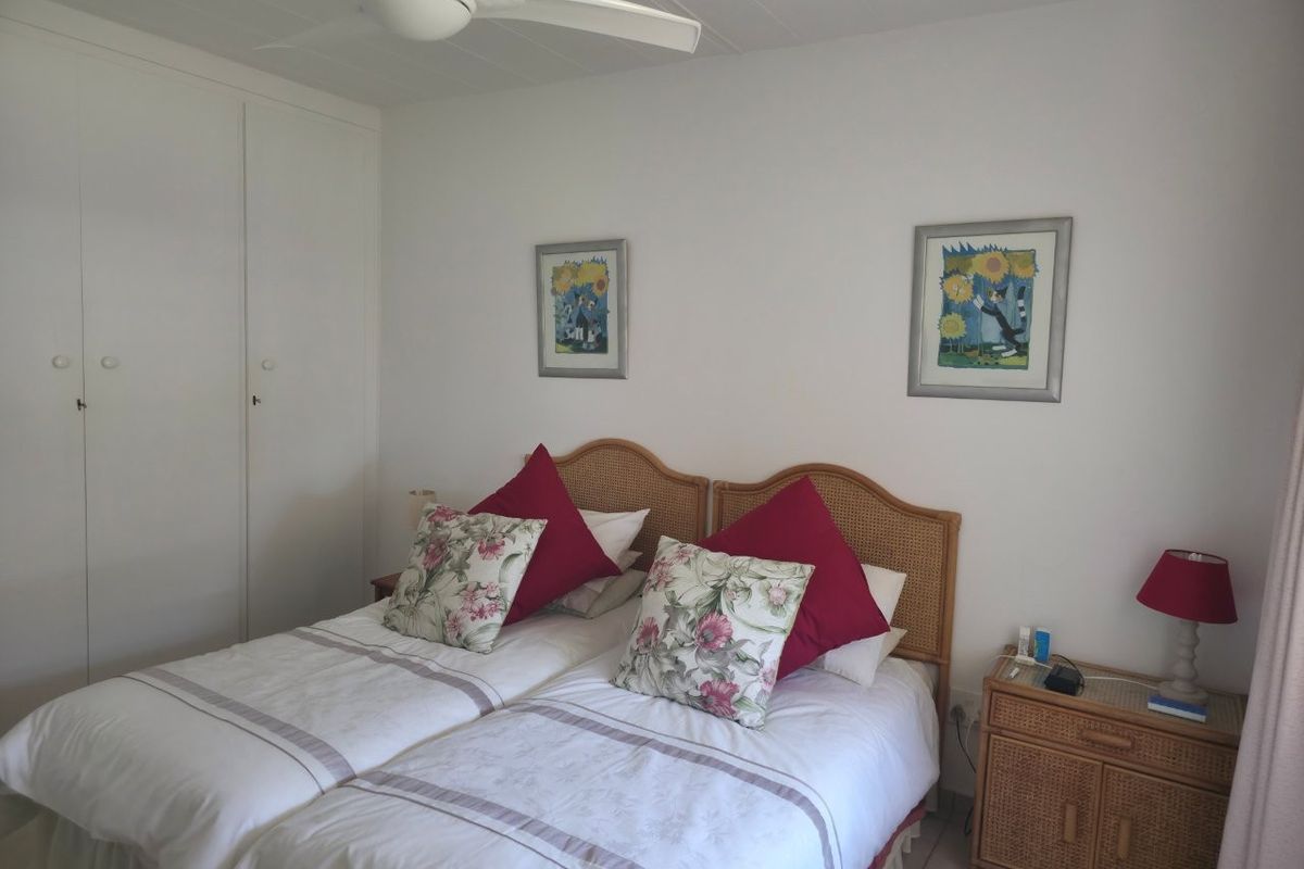 A functional bedroom featuring built-in wardrobes, a ceiling fan, and tiled flooring, offering a clean and neutral space.