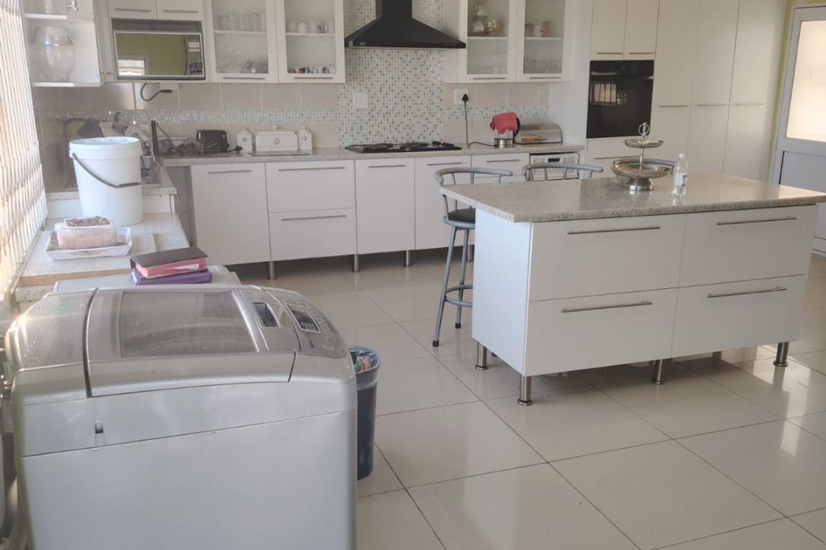 Modern kitchen featuring white cabinetry, a central island with stone countertops, integrated appliances, and a mosaic tile backsplash with tiled flooring.