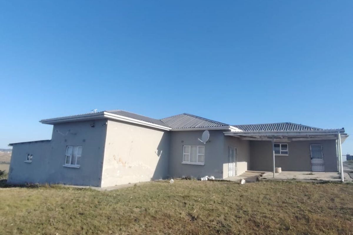 Rear view of a single-story house featuring a covered patio area, tiled roof, and exterior walls showing signs of wear and paint deterioration.