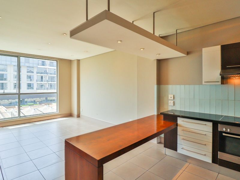 Modern open-plan kitchen and living area featuring sleek cabinetry, integrated appliances, a breakfast bar, and large windows providing ample natural light.
