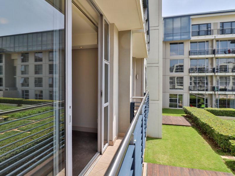 A modern apartment balcony featuring a metal balustrade, tiled flooring, and a large sliding glass door providing access to the interior.