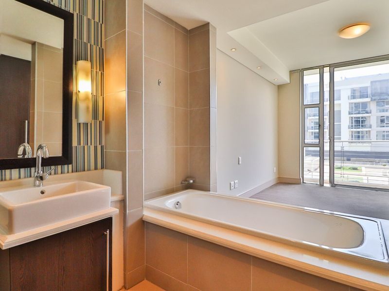 Modern bathroom featuring a built-in vanity with basin, a tiled bathtub, and direct access to a balcony through sliding glass doors.