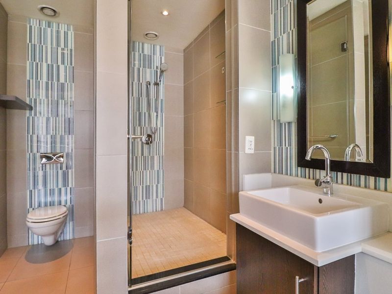 Modern bathroom featuring a glass-enclosed shower, wall-mounted toilet, and a vanity basin with a framed mirror and decorative tiled accents.
