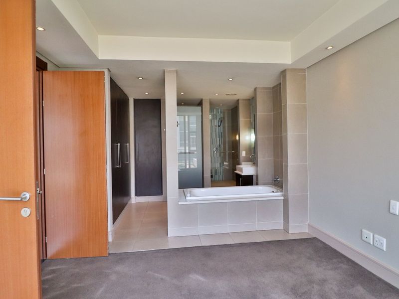 Spacious bedroom featuring an open-plan en-suite bathroom with a built-in bathtub, vanity basin, and ample built-in cupboard storage.