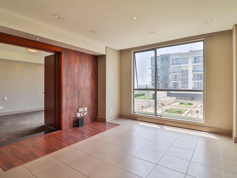 A bright, empty living area featuring tiled floors, a timber accent wall, and large windows offering an urban view.