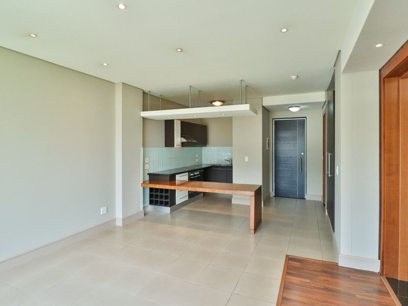 An open-plan living and kitchen area featuring tiled floors, recessed lighting, and a modern kitchen with a built-in breakfast bar and integrated appliances.