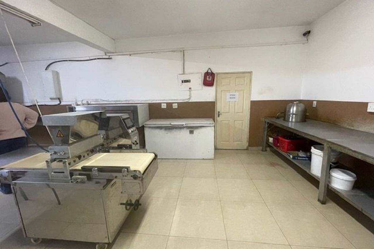 Commercial kitchen space featuring tiled flooring, stainless steel prep surfaces, and functional access door, suitable for food preparation or utility operations.