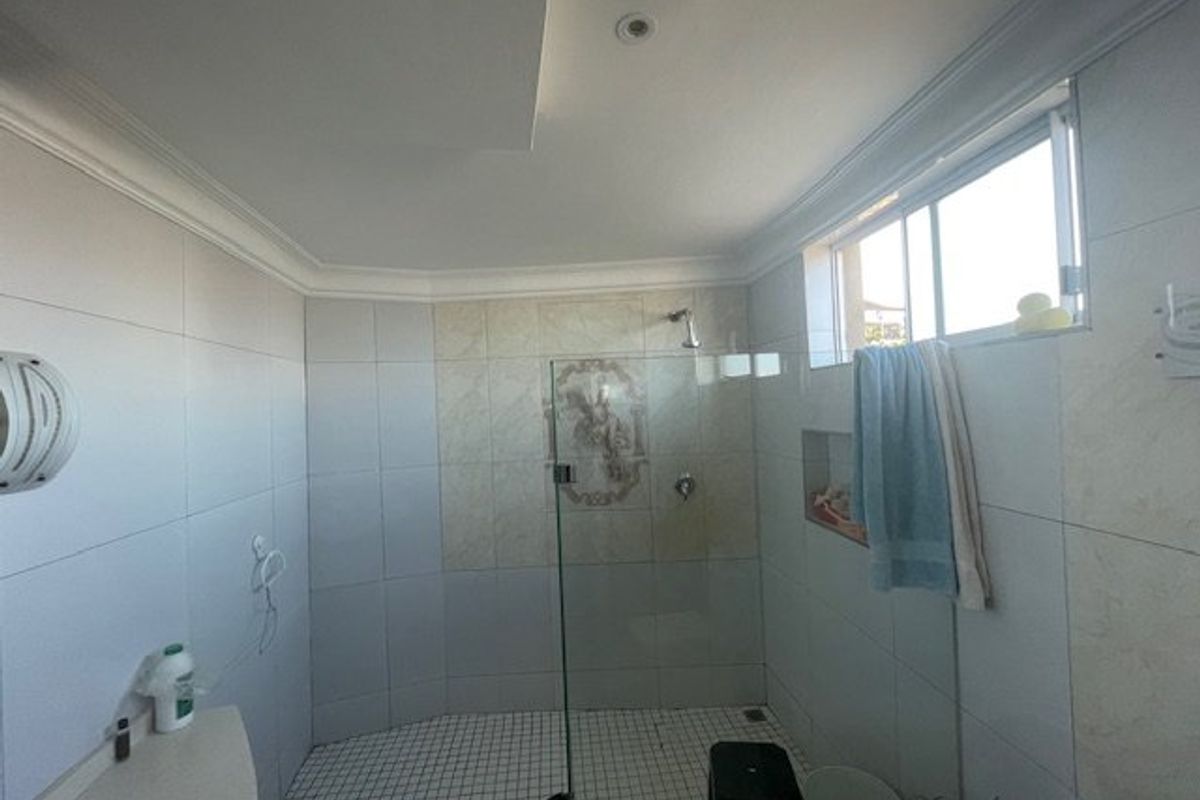 A functional bathroom featuring a glass-enclosed shower, tiled walls and flooring, and a recessed wall niche for storage.