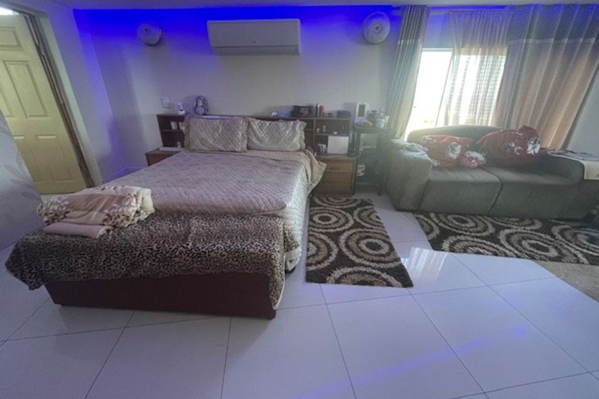 Spacious bedroom featuring tiled flooring, a built-in headboard, and a wall-mounted split-system air conditioning unit with integrated ambient lighting.