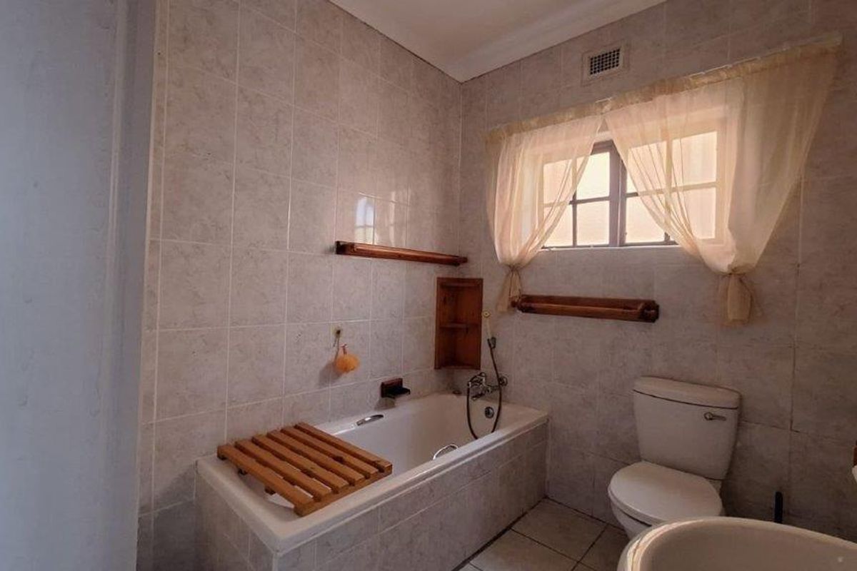A functional bathroom featuring a built-in bathtub, toilet, and basin with neutral wall and floor tiling.