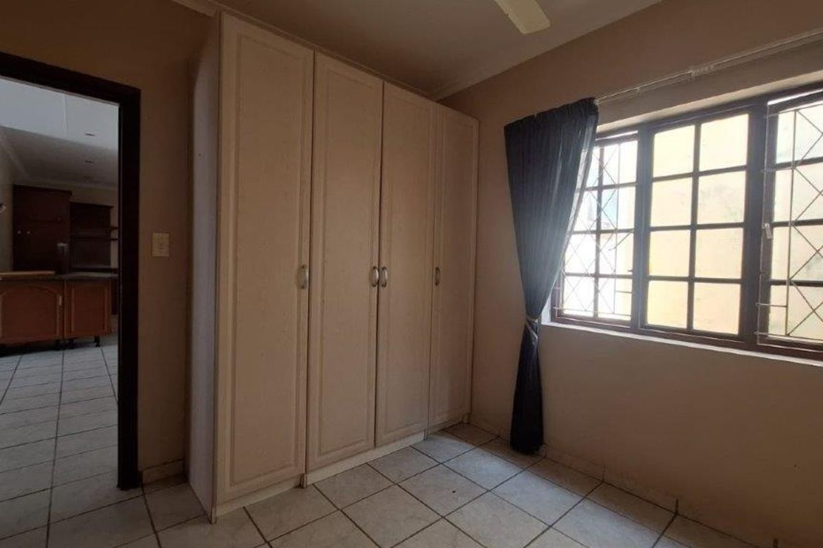 A bedroom featuring built-in cupboards, tiled flooring, and a window with security bars, offering a functional and neutral space.
