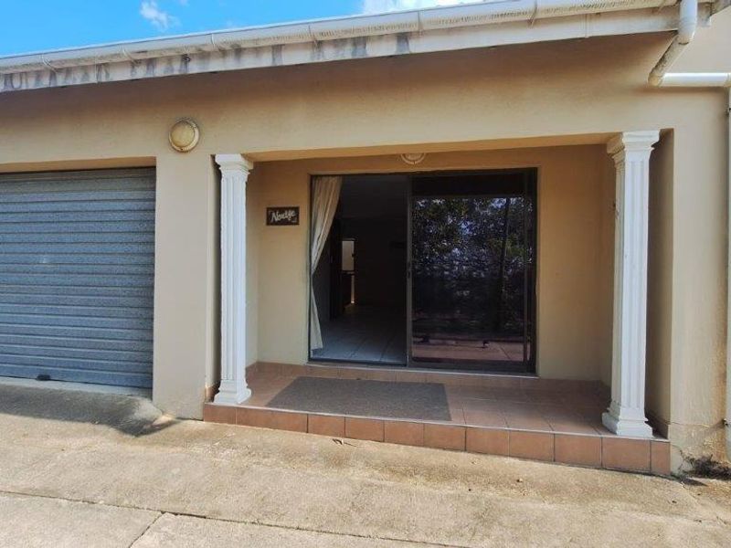 Front exterior view of the townhouse featuring a single roller garage door, a covered tiled patio entrance, and sliding glass door access.