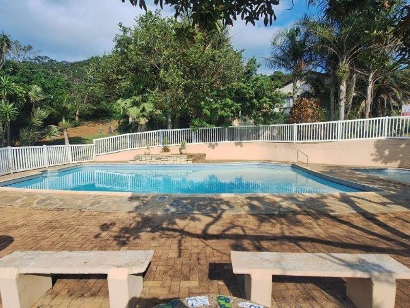 Outdoor pool area featuring a swimming pool, paved deck, and white perimeter fencing, set within a landscaped garden environment.