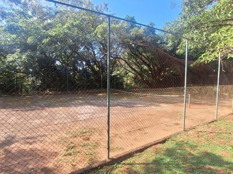 A private tennis court facility featuring chain-link perimeter fencing, currently showing signs of significant wear and maintenance requirements.