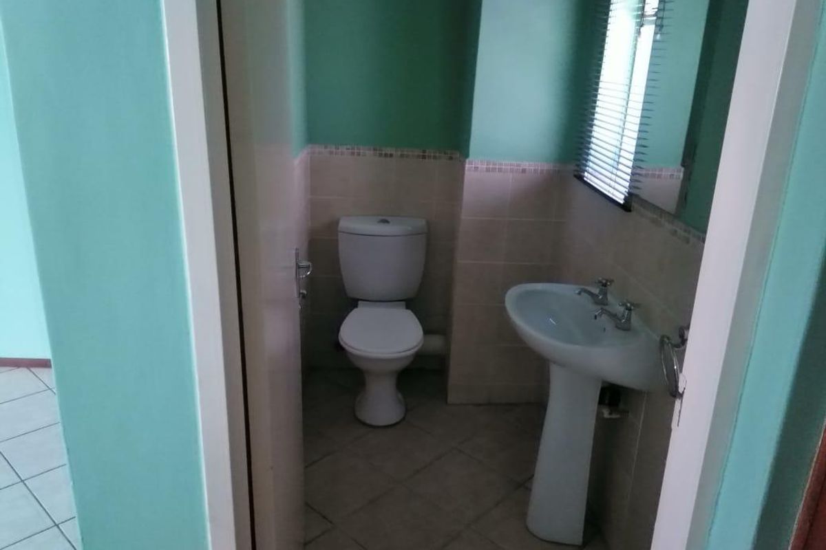 A compact bathroom featuring a pedestal basin, toilet, tiled flooring, and neutral wall tiling.