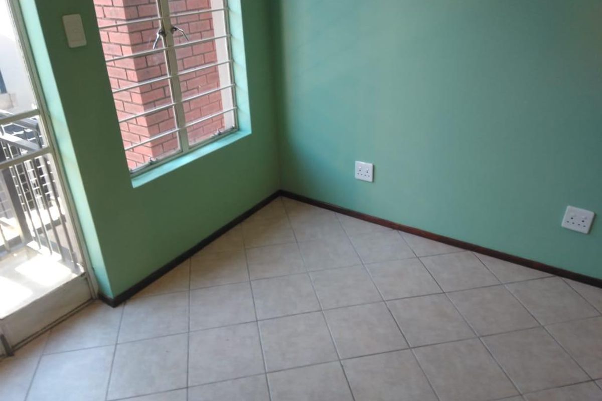 An empty bedroom featuring tiled flooring, green painted walls, and a sliding door leading to an outdoor area with security bars.