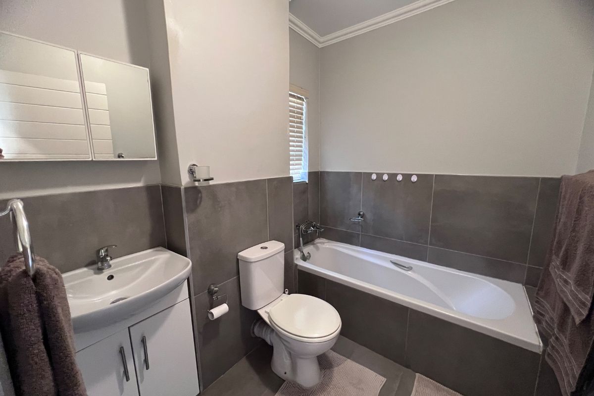 A modern bathroom featuring a vanity cabinet with basin, a toilet, and a bathtub with tiled wall finishes.