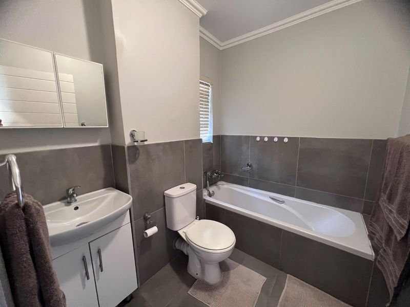 A modern bathroom featuring a vanity cabinet with basin, a toilet, and a bathtub with tiled wall finishes.