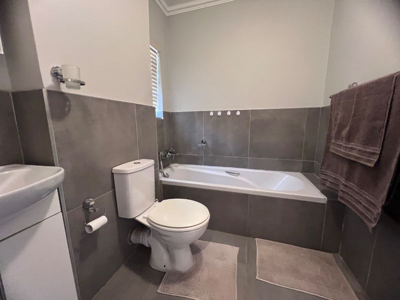 A functional bathroom featuring a built-in bathtub, toilet, and vanity basin with modern grey wall and floor tiling.