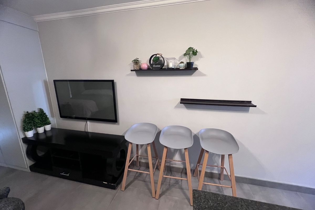 A living area featuring tiled flooring, crown molding, and wall-mounted shelving, providing a clean and functional space for relaxation.