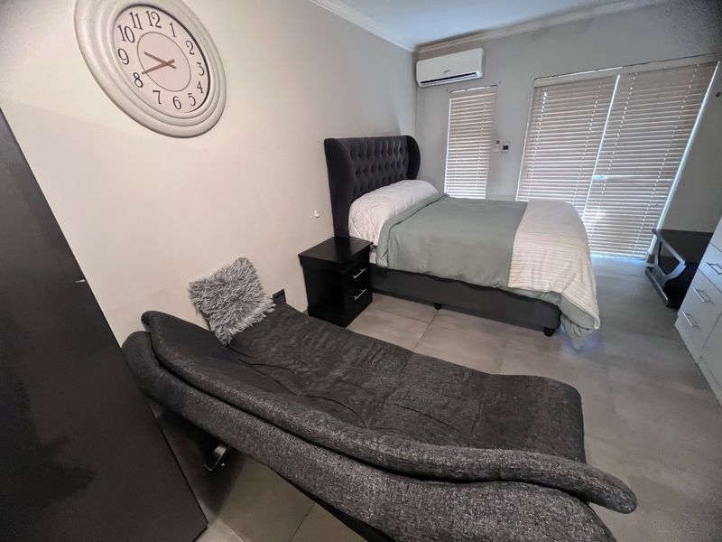 A well-maintained bedroom featuring tiled flooring, an integrated air conditioning unit, and venetian blinds covering the sliding door access.