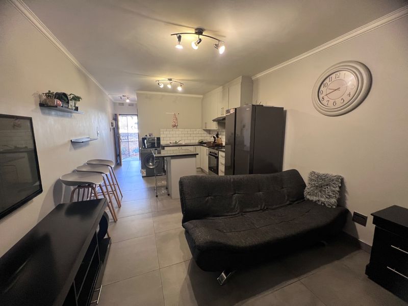 An open-plan living and kitchen area featuring tiled floors, modern cabinetry, subway tile backsplash, and integrated cooking appliances.