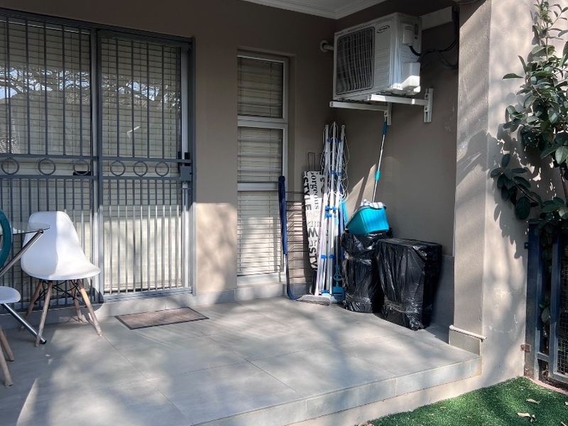 A covered patio area featuring tiled flooring, a security gate, and a wall-mounted air conditioning unit.