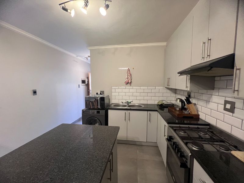 Modern kitchen featuring granite countertops, subway tile backsplash, gas stove with extractor fan, and ample built-in cabinetry.