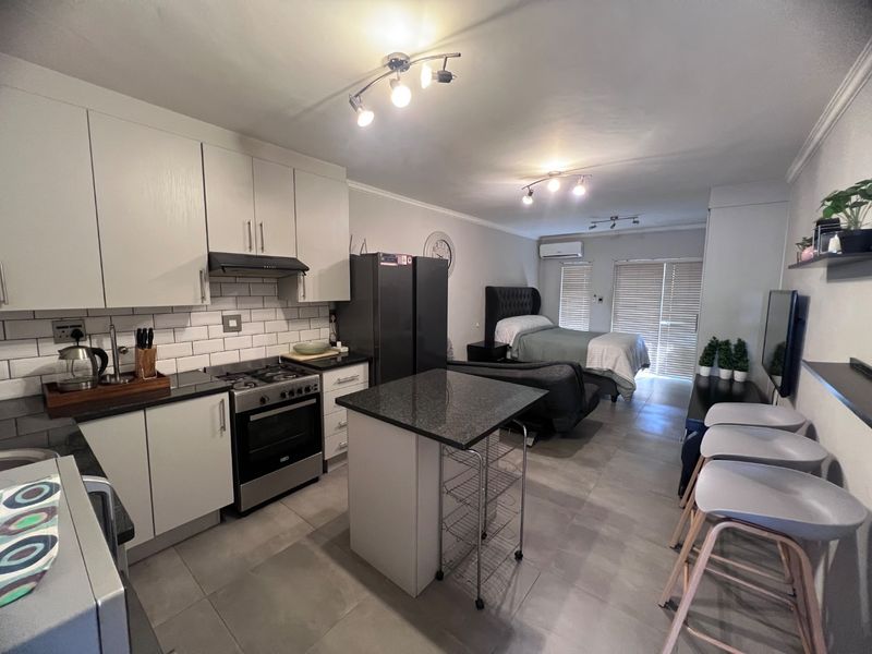Modern open-plan studio apartment featuring a well-equipped kitchen with granite countertops, subway tile backsplash, and a seamless transition to the bedroom and living area.