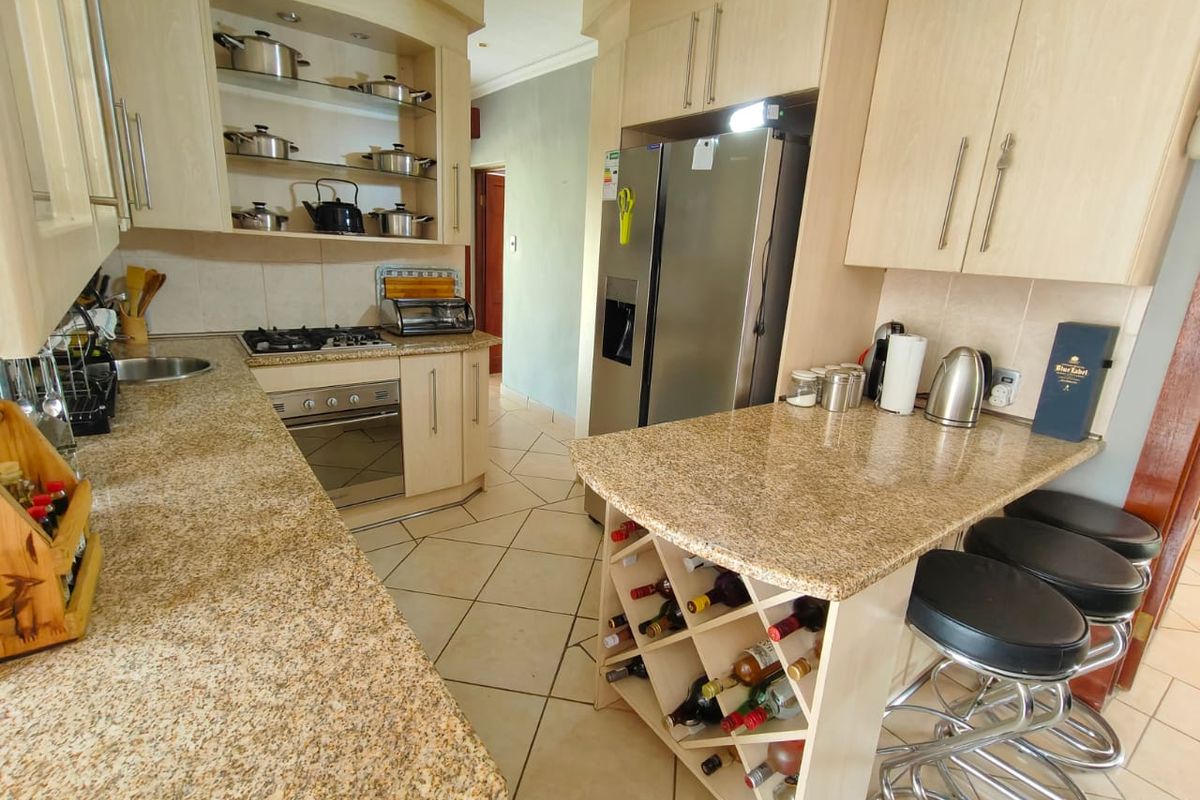 A functional kitchen featuring granite countertops, light wood cabinetry, a built-in gas hob, oven, and a convenient breakfast bar with integrated wine storage.