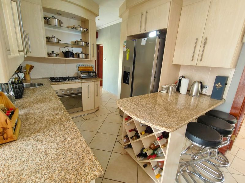 A functional kitchen featuring granite countertops, light wood cabinetry, a built-in gas hob, oven, and a convenient breakfast bar with integrated wine storage.