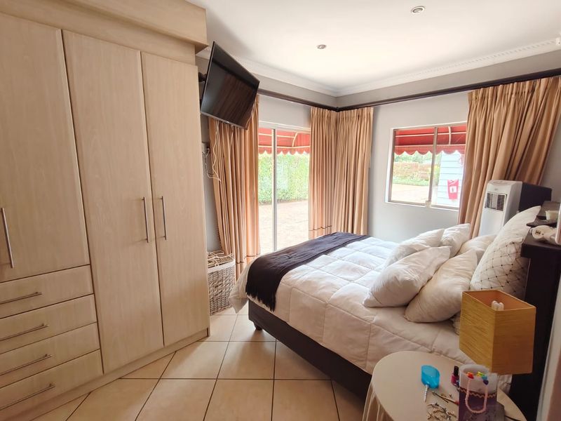 A well-maintained bedroom featuring light wood built-in cupboards, tiled flooring, recessed lighting, and direct access to the garden through a sliding glass door.
