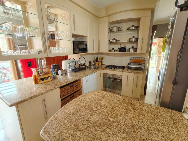 A functional kitchen featuring light wood cabinetry, granite countertops, a built-in oven, gas hob, and glass-fronted display cabinets for storage.