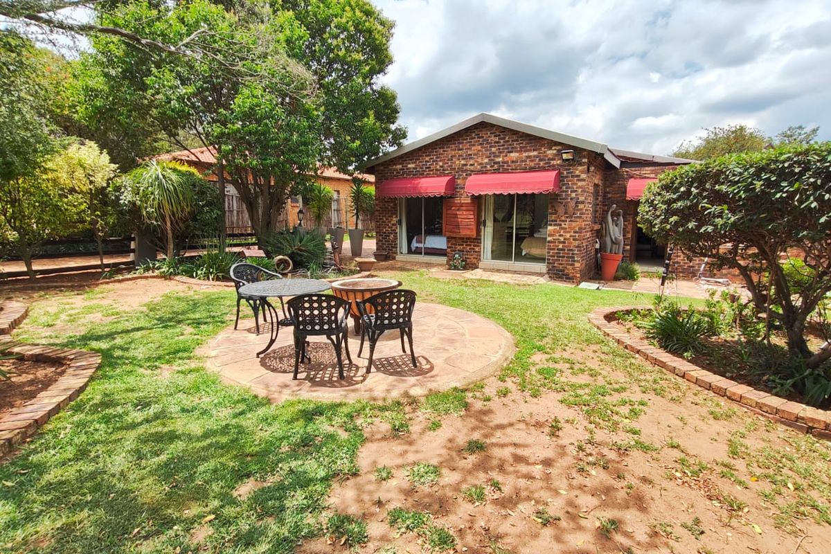 Rear view of a brick house featuring a paved patio area, landscaped garden, and sliding glass doors with red awnings.