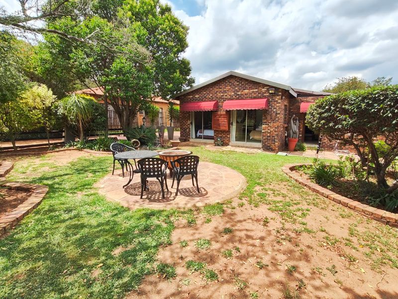 Rear view of a brick house featuring a paved patio area, landscaped garden, and sliding glass doors with red awnings.