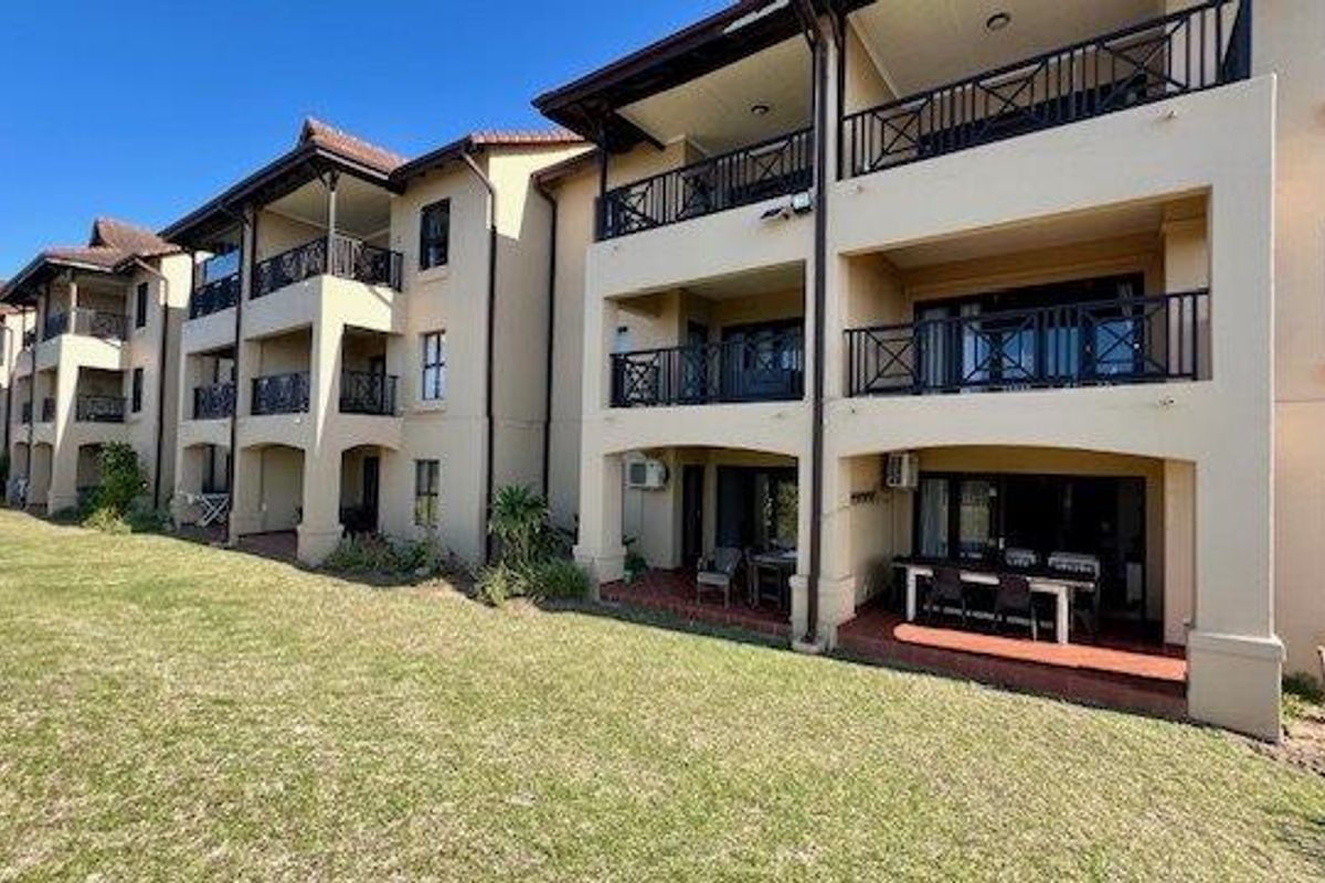 Rear view of a multi-story apartment complex featuring private balconies with metal railings and ground-floor patio areas overlooking a communal lawn.