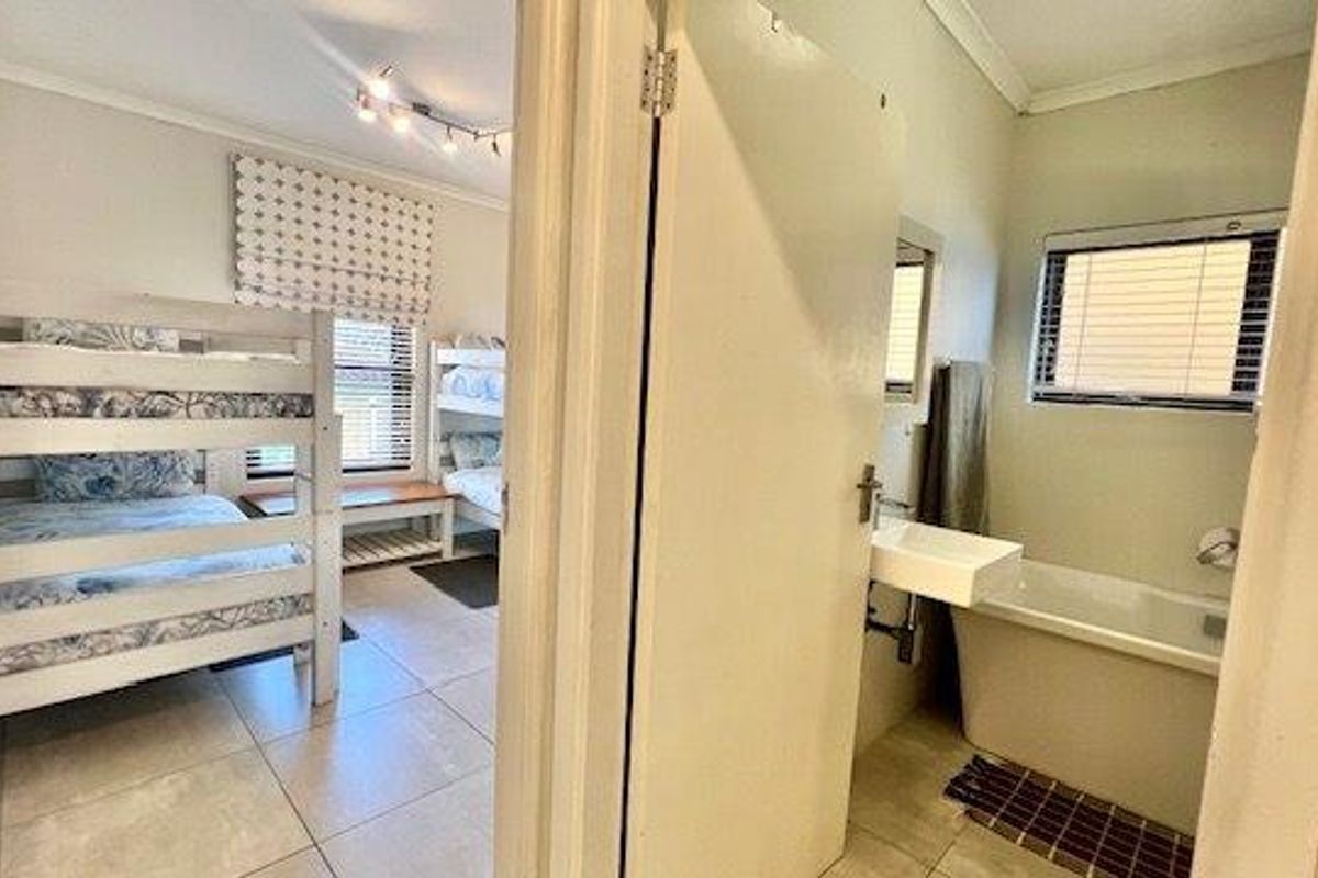 A bedroom featuring tiled flooring and an adjacent bathroom equipped with a wall-mounted basin and a bathtub.