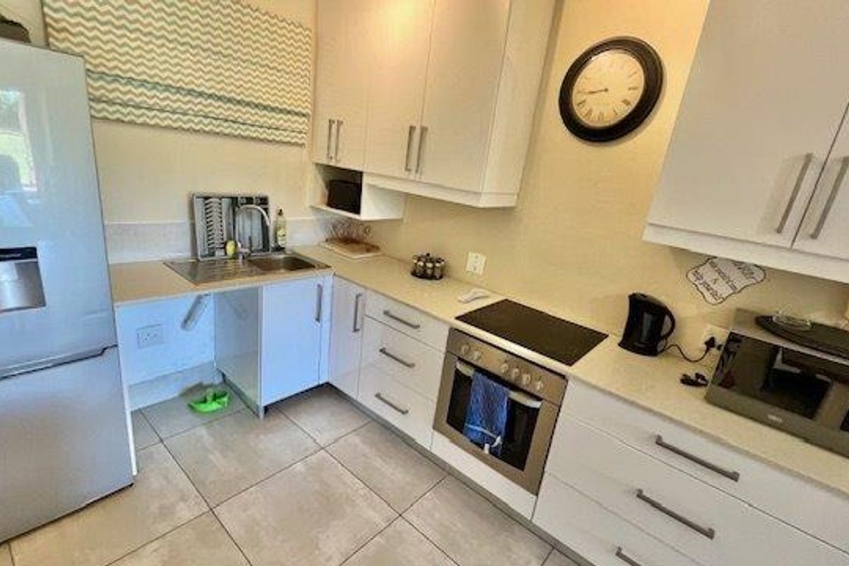 A functional kitchen featuring white cabinetry, stone countertops, integrated oven and hob, and tiled flooring.