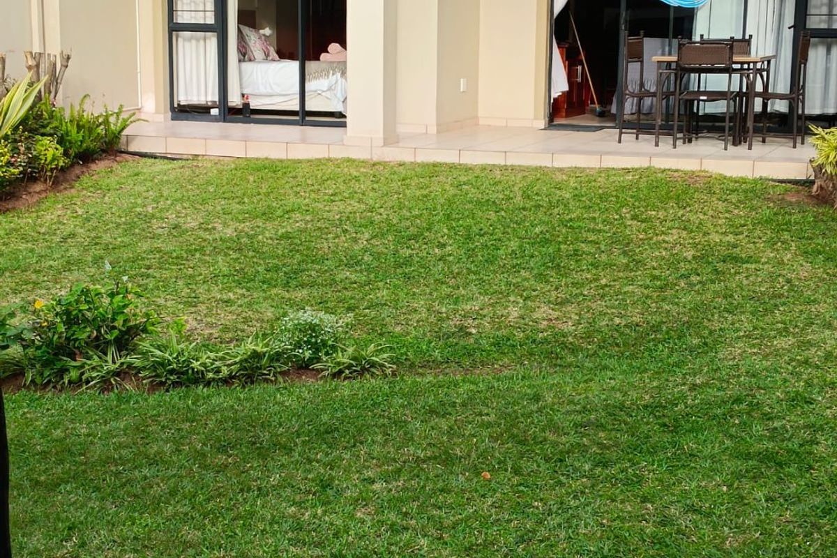 A ground floor apartment featuring a private lawn, landscaped garden beds, and a tiled patio with sliding door access to the interior.