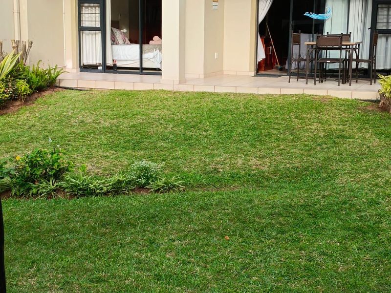A ground floor apartment featuring a private lawn, landscaped garden beds, and a tiled patio with sliding door access to the interior.