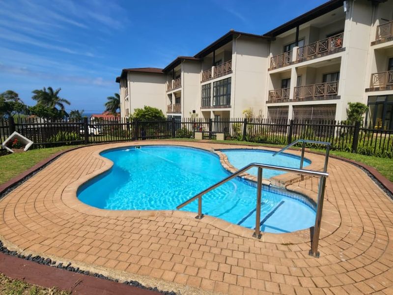 A well-maintained communal swimming pool area featuring paved decking and metal handrails, set against a multi-story apartment complex with balcony access.