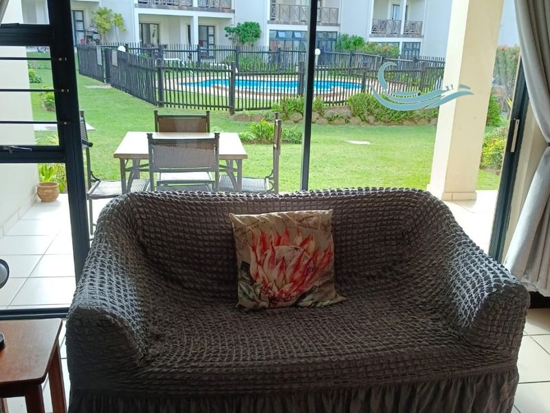 Living room featuring large sliding glass doors that provide direct access to a patio and views of the complex garden and pool area.
