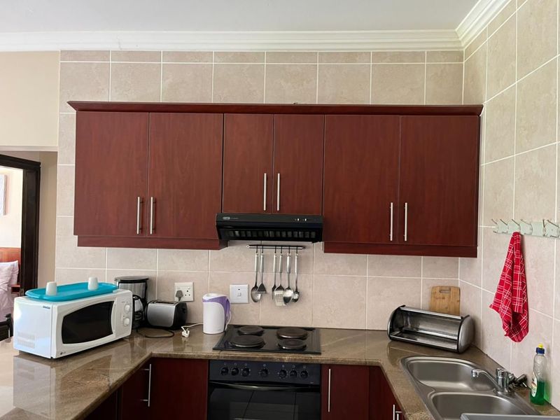 A functional kitchen featuring dark wood cabinetry, granite countertops, a built-in oven with hob, extractor fan, and a double bowl sink with tiled backsplash.