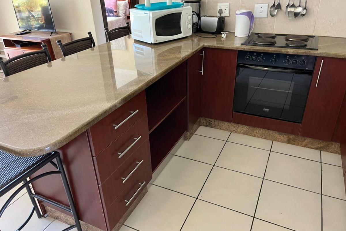 A functional kitchen featuring dark wood cabinetry, granite countertops, a built-in oven, and an electric hob with tiled flooring and backsplash.