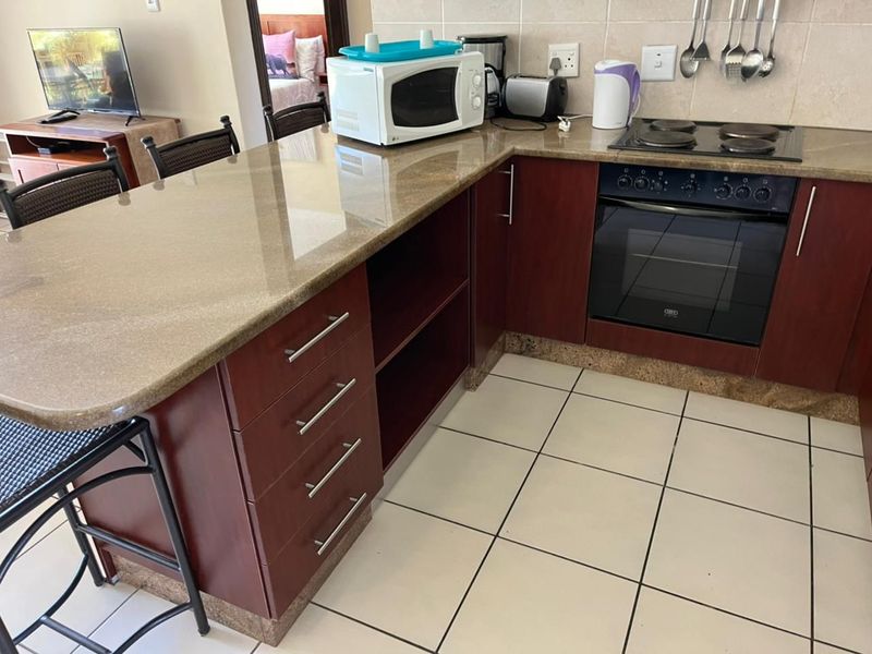 A functional kitchen featuring dark wood cabinetry, granite countertops, a built-in oven, and an electric hob with tiled flooring and backsplash.