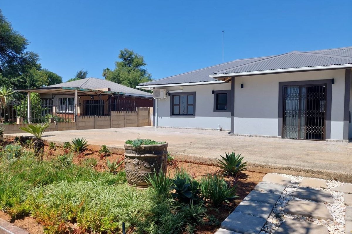 Rear view of the property featuring a concrete patio, landscaped garden, and a well-maintained building exterior with a metal roof.
