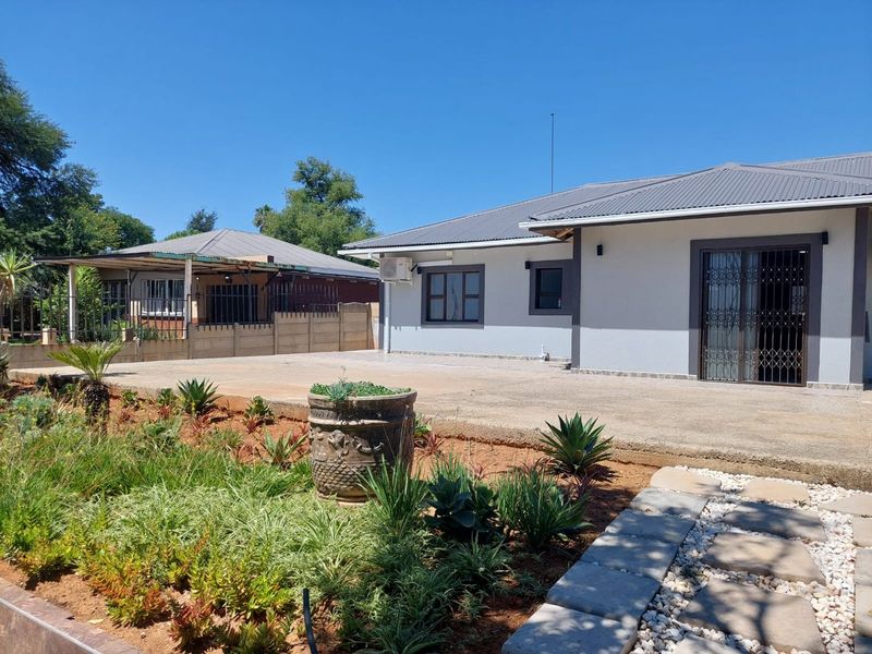 Rear view of the property featuring a concrete patio, landscaped garden, and a well-maintained building exterior with a metal roof.