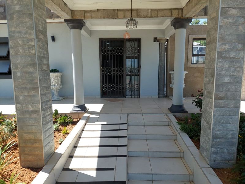 Covered entrance porch featuring tiled steps, decorative concrete columns, and stone-clad pillars leading to a secure metal entrance gate.