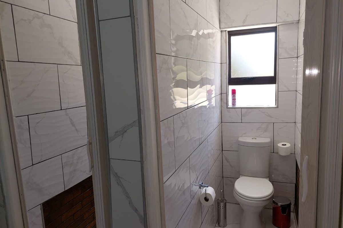 A compact, modern bathroom featuring white marble-effect wall tiles, tiled flooring, and a standard toilet suite.
