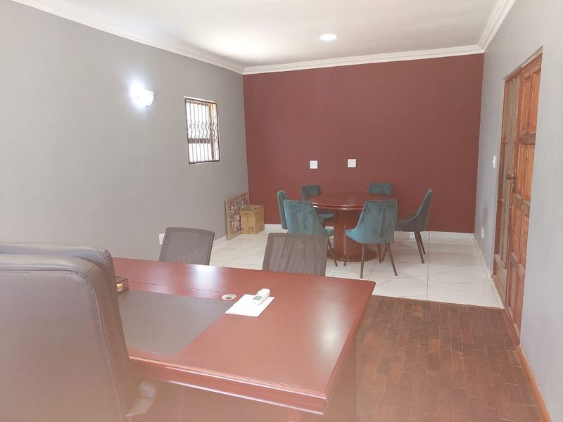 A functional office space featuring a mix of tiled and wooden flooring, recessed lighting, and a secure window with security bars.